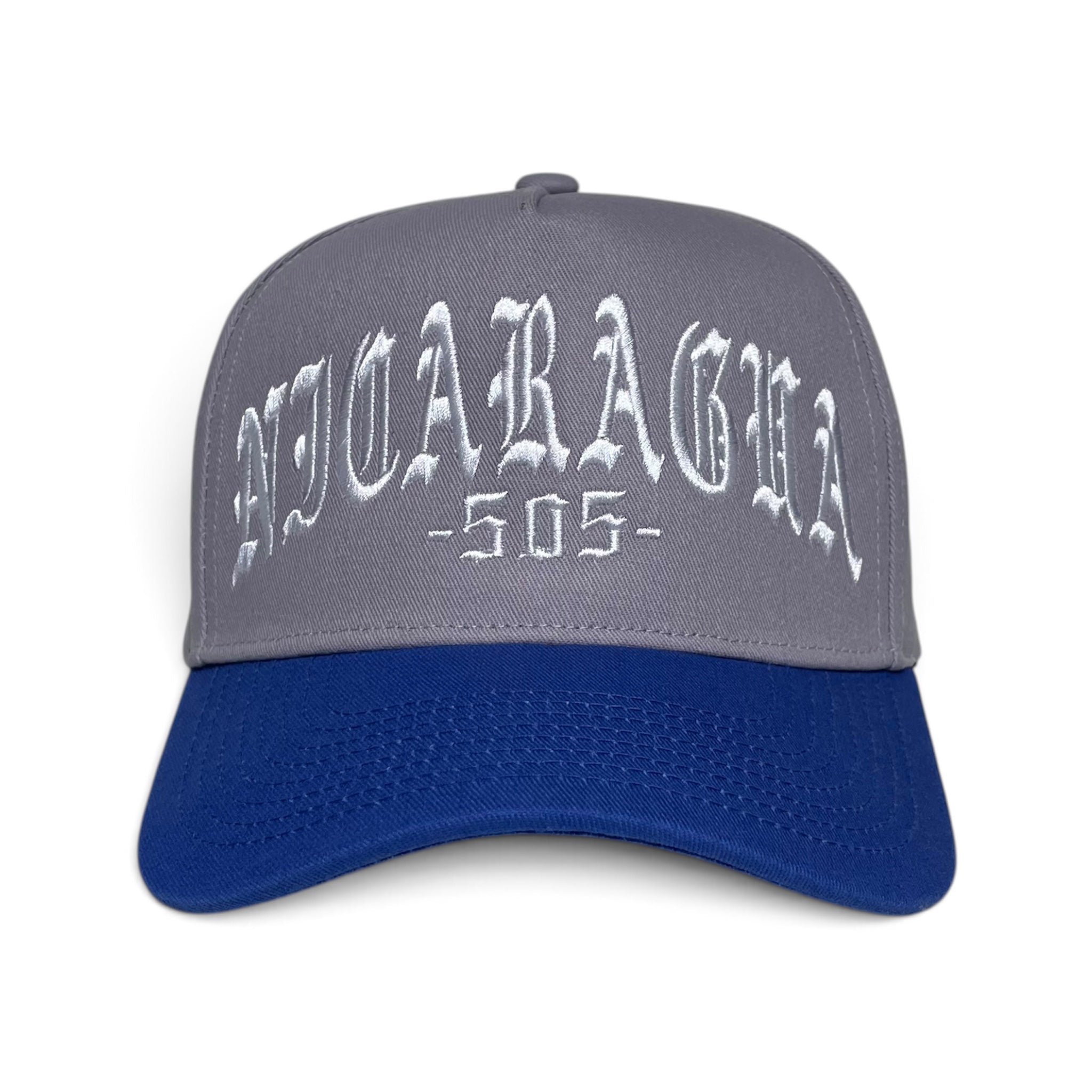 A baseball cap with a gray crown, white embroidered gothic-style 'NICARAGHA -505-' text, and a royal blue curved brim, shown against a plain white background.